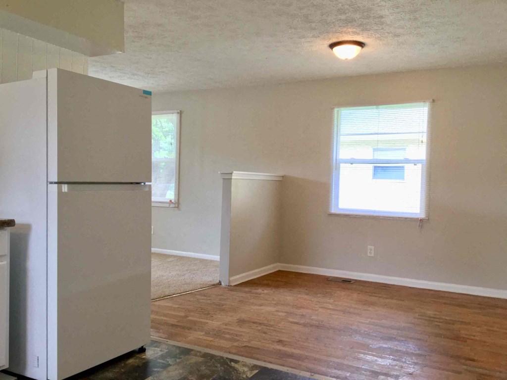 an empty living room with a refrigerator and a window