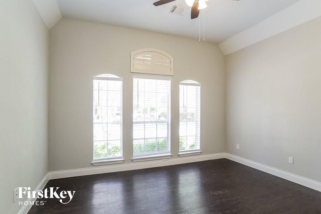 an empty living room with three windows and a ceiling fan