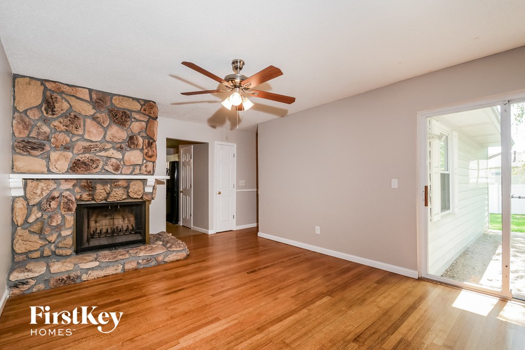 an empty living room with a stone fireplace and a ceiling fan