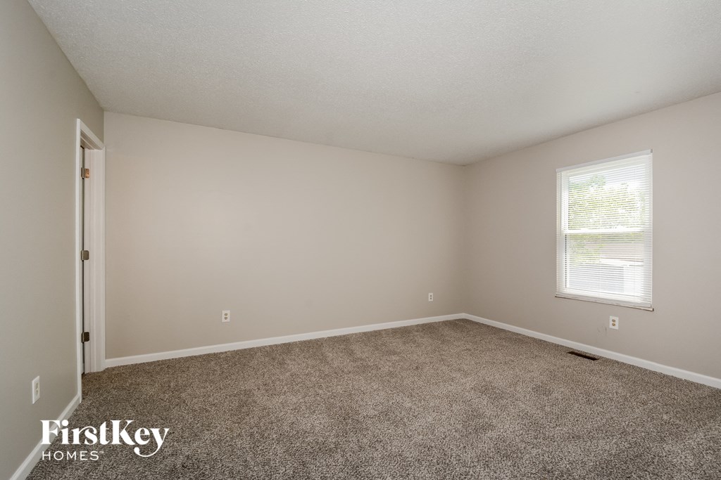 the spacious bedroom with carpeted flooring and a window