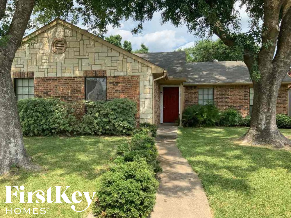 A brick house with a red door and a tree in front.