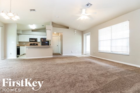 an empty living room with carpet and a kitchen