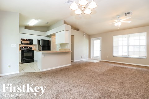 an empty living room with a kitchen in the corner
