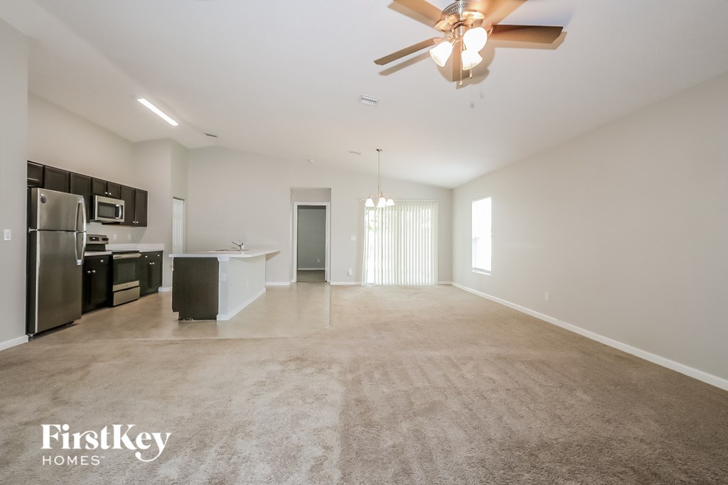 an empty living room with a ceiling fan and a kitchen