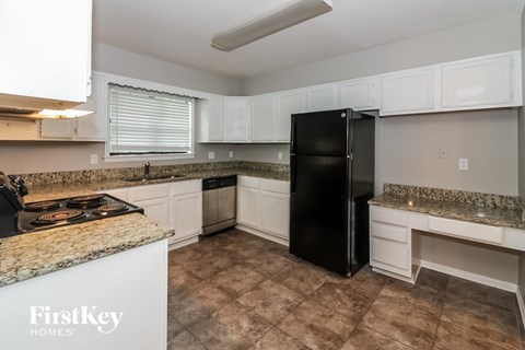 a kitchen with white cabinets and granite counter tops and a black refrigerator