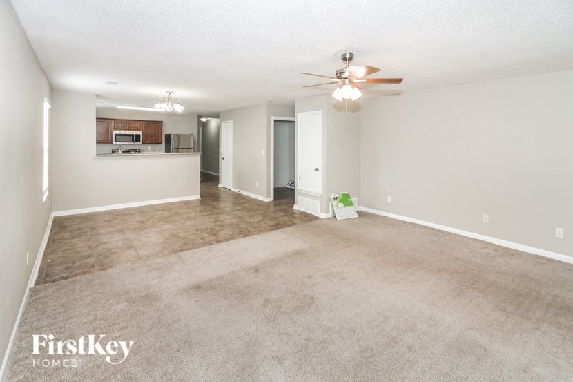 an empty living room with a ceiling fan and a kitchen