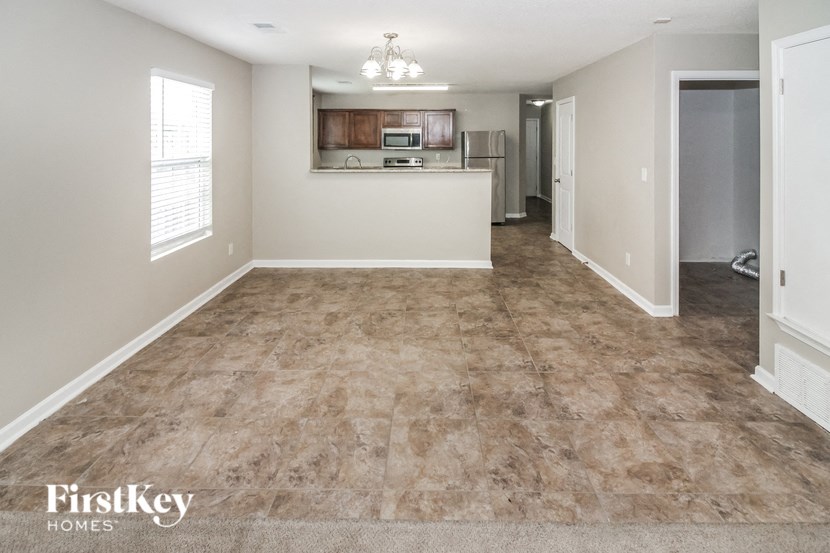 an empty living room with a kitchen in the background