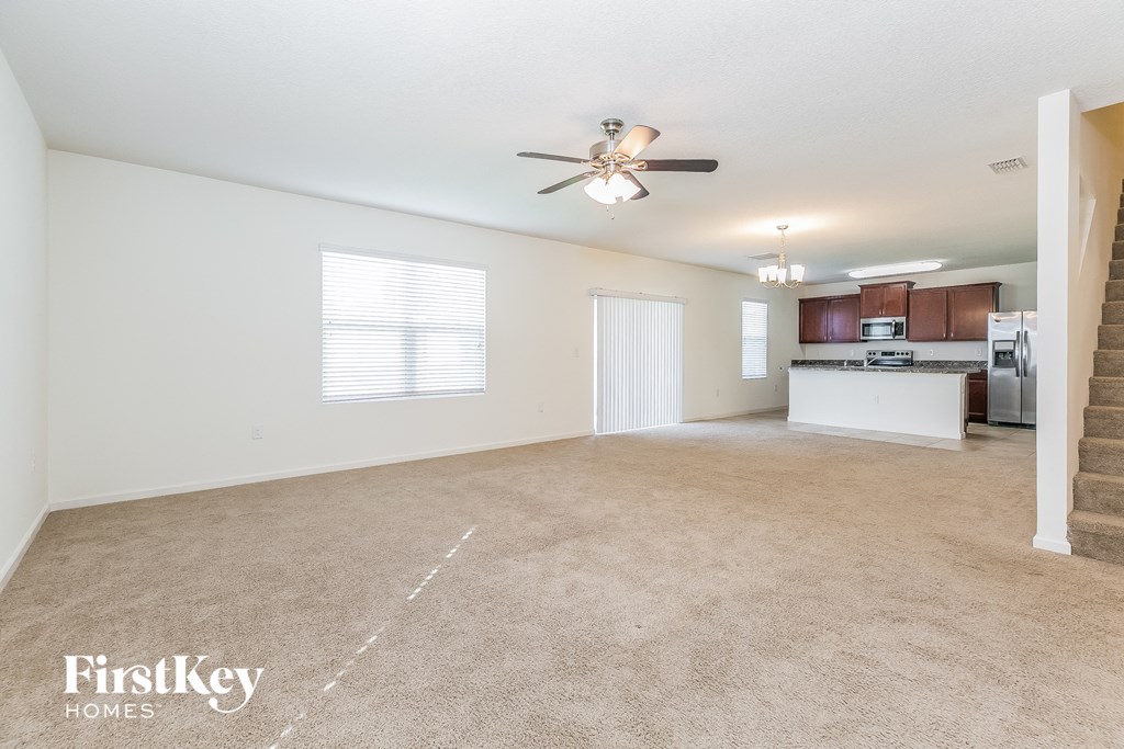 A spacious living room with a carpeted floor and a ceiling fan.