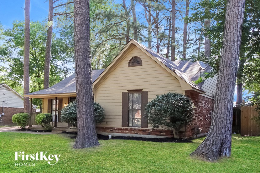 A house with a yellow siding and a brown roof is surrounded by trees.