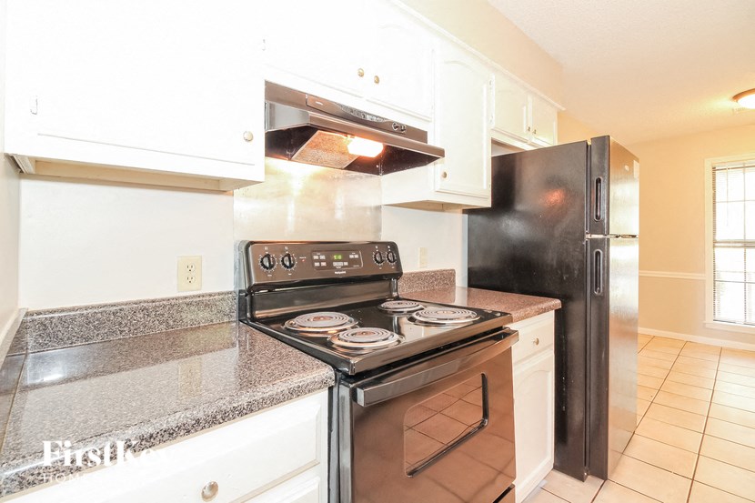 A black refrigerator is in a kitchen with white cabinets.