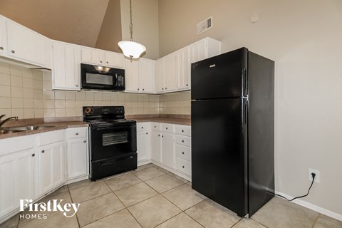 A black refrigerator stands in a kitchen with white cabinets and a black oven.