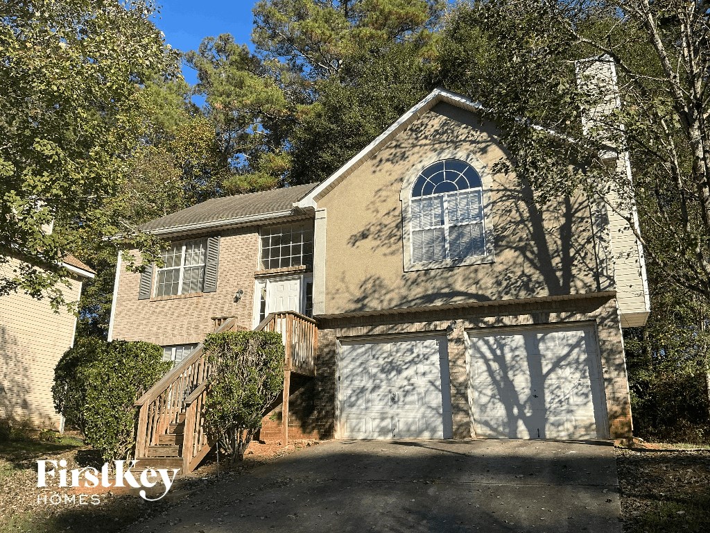 A house with a garage door and a window is surrounded by trees.