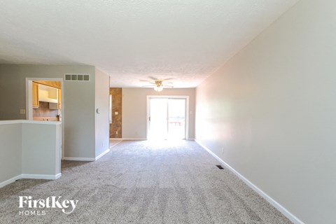 A carpeted room with a white wall and a doorway leading to another room.