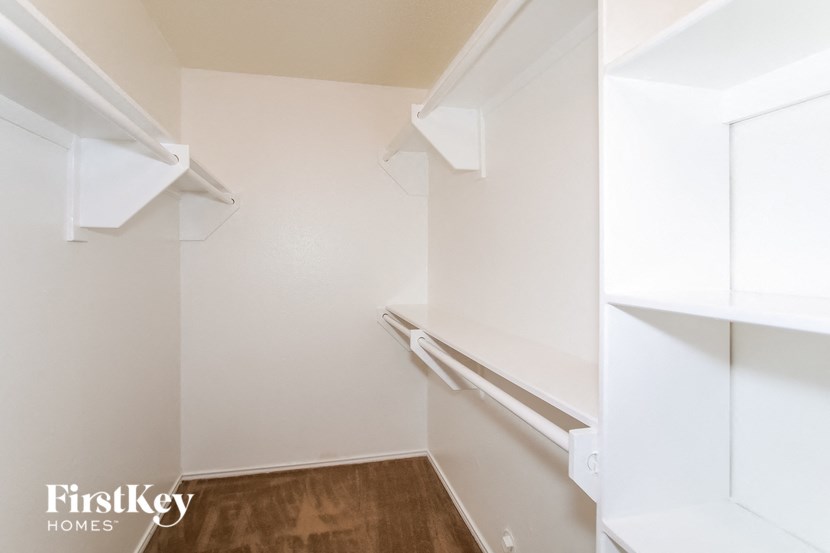 a walk in closet with white shelves and a wood floor