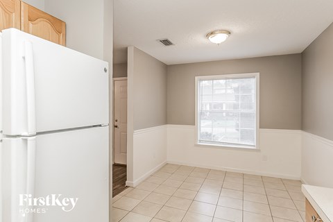 A white refrigerator is in a kitchen with white tile flooring and a window.