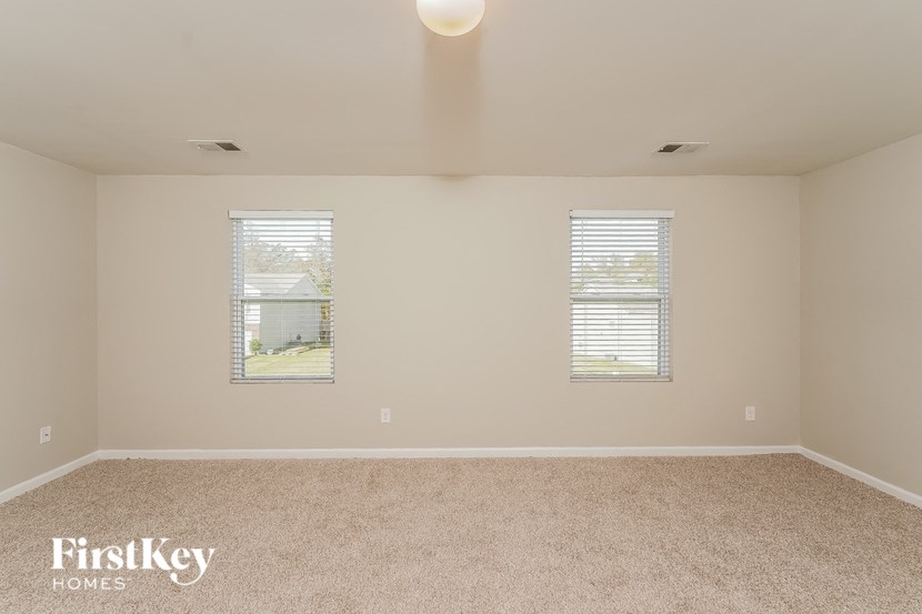 A room with a carpeted floor and two windows.