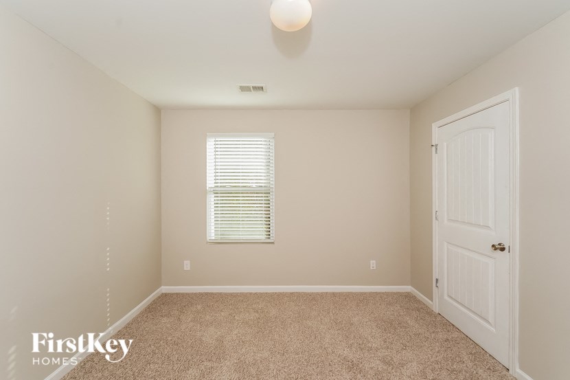 A room with a carpeted floor, a window with blinds, a door, and a FirstKey Homes logo.