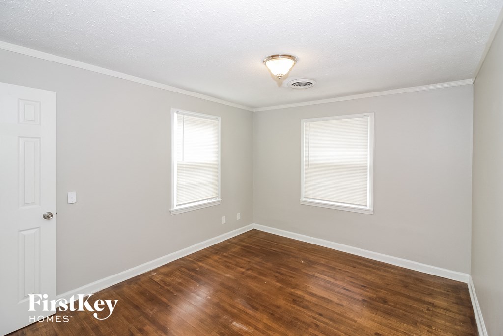 a bedroom with a hard wood floor and two windows