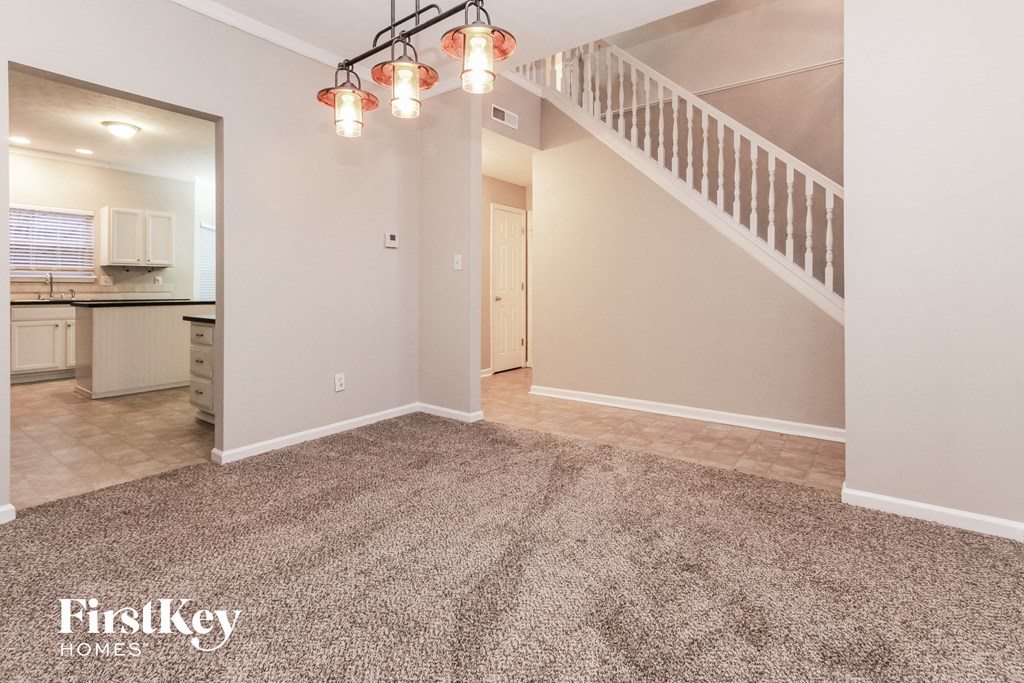 the living room and dining room of a house with carpet and a staircase