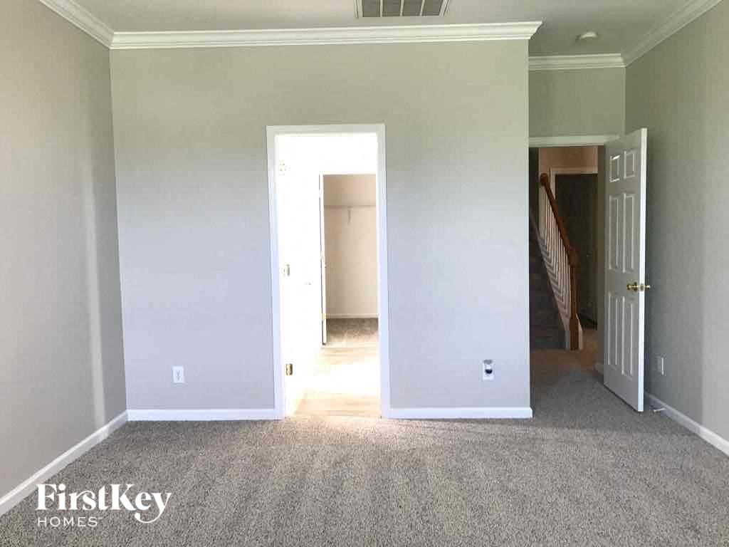 an empty living room with white carpet and a door to a hallway