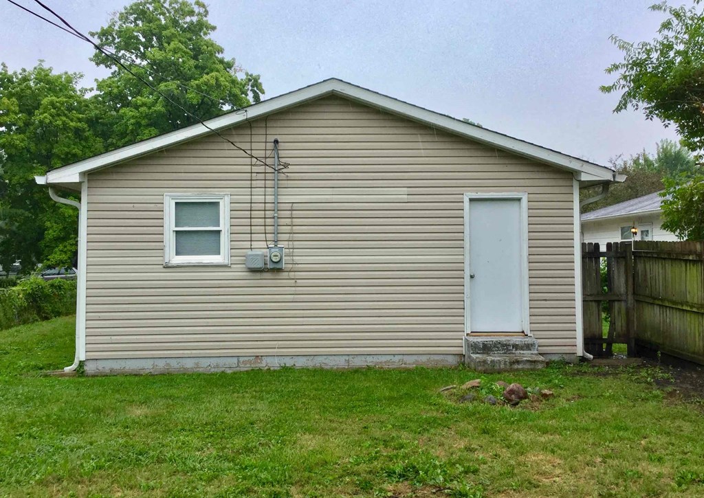 A small house with a white door and a window is surrounded by grass and trees.