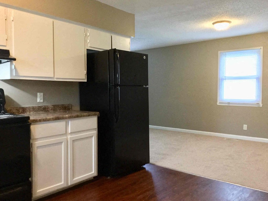 A black refrigerator stands in a kitchen with white cabinets.