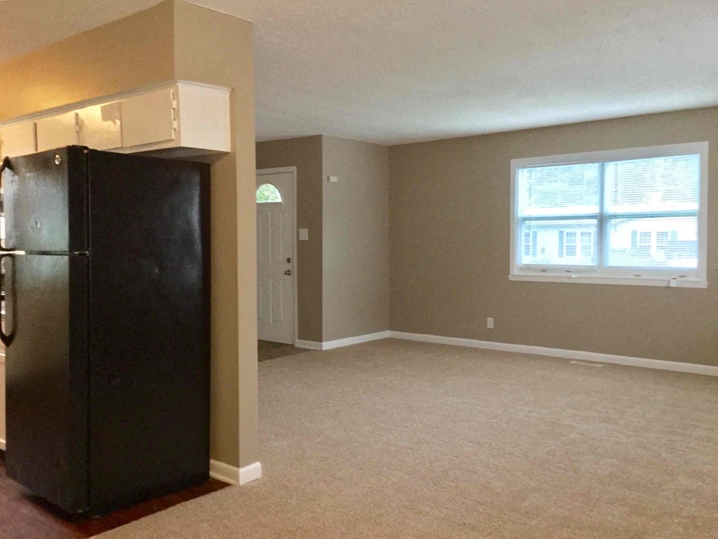 A black refrigerator stands in a room with beige walls and carpeting.
