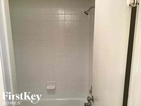 A white tiled shower with a shower head and a white door.