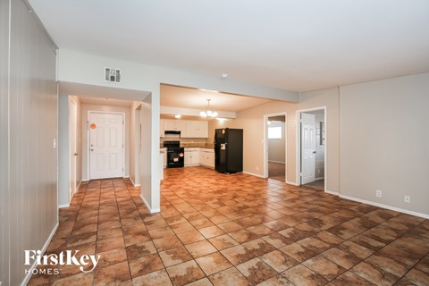A spacious living room with a tile floor and a kitchen area in the background.