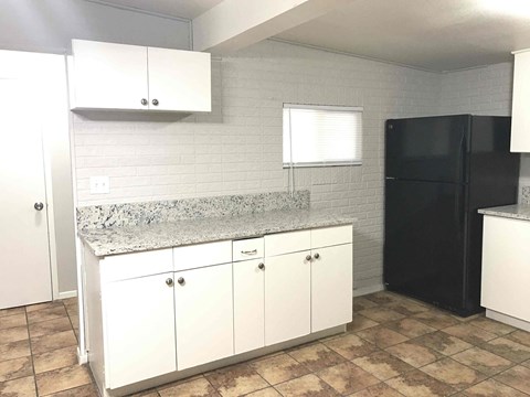 A kitchen with white cabinets and a black refrigerator.