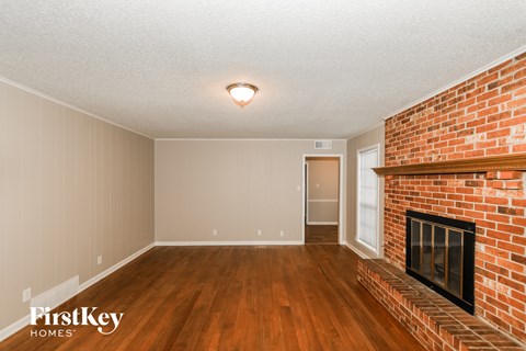 A room with a brick fireplace and wood flooring.
