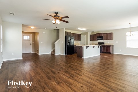 an empty living room and kitchen with wood flooring and a ceiling fan