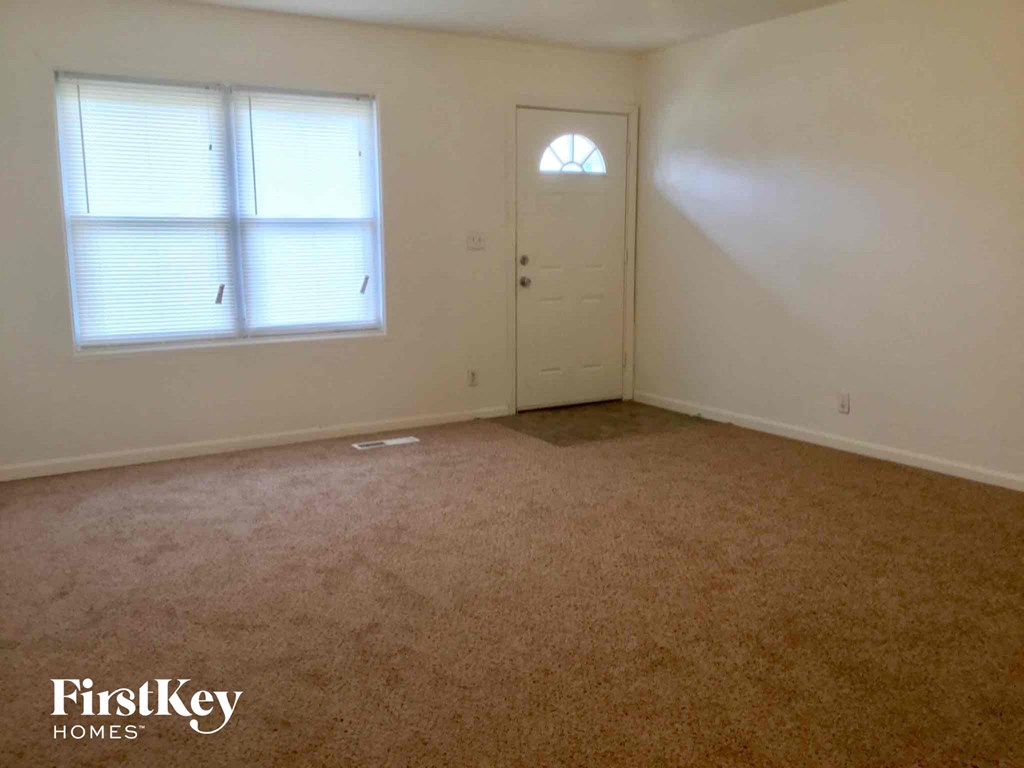 A room with a carpeted floor, a door, and a window with blinds.