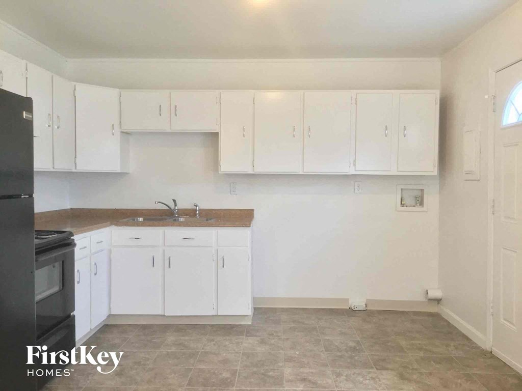 A kitchen with white cabinets and a black fridge.