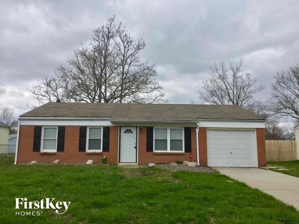 A brick house with a white garage door and a tree in front of it.