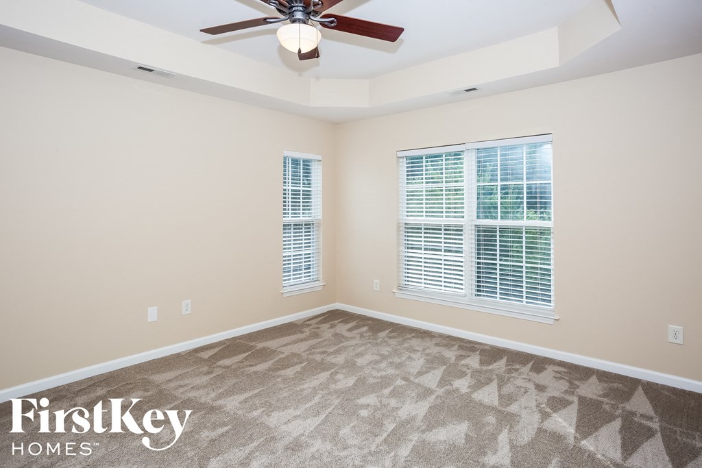 A room with a carpet floor, a ceiling fan, and a window with blinds.