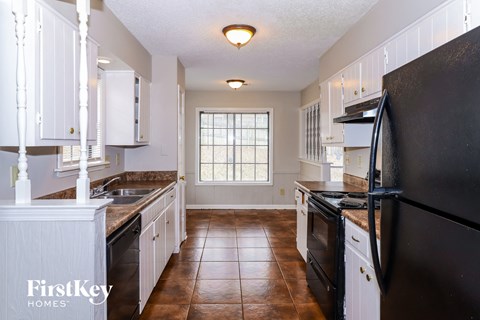 A kitchen with black appliances and brown tile flooring.