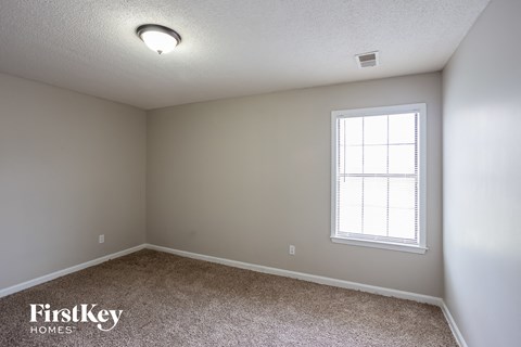 the spacious bedroom with carpeted flooring and a window