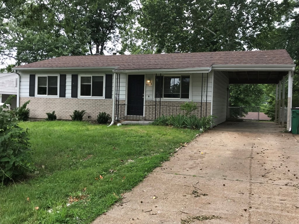 A small house with a black door and windows is surrounded by greenery.