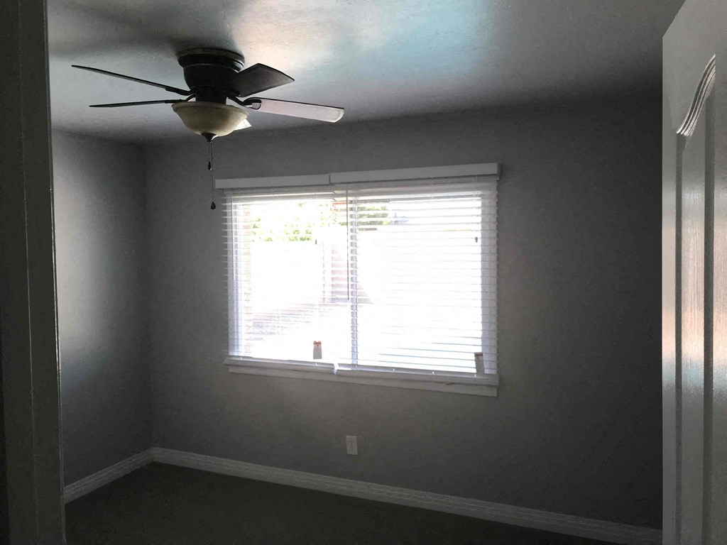 A room with a ceiling fan and a window with blinds.