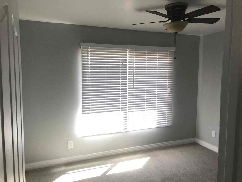 A room with a ceiling fan and a window with blinds.