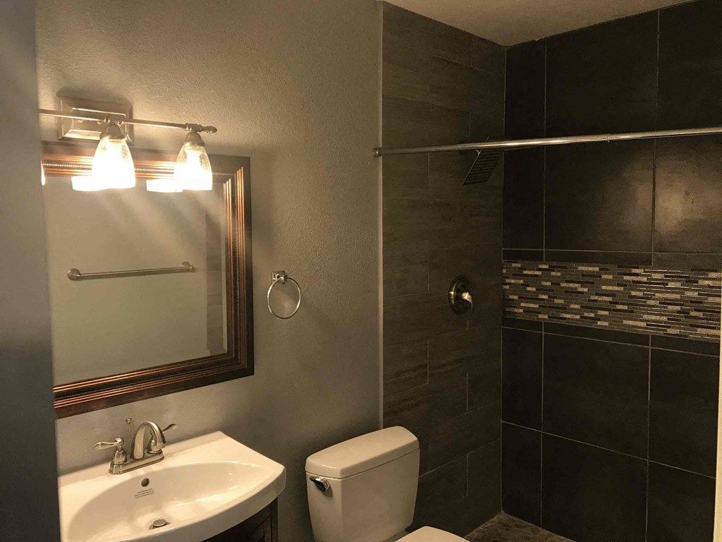 A bathroom with a toilet, sink, mirror, and tiled walls.