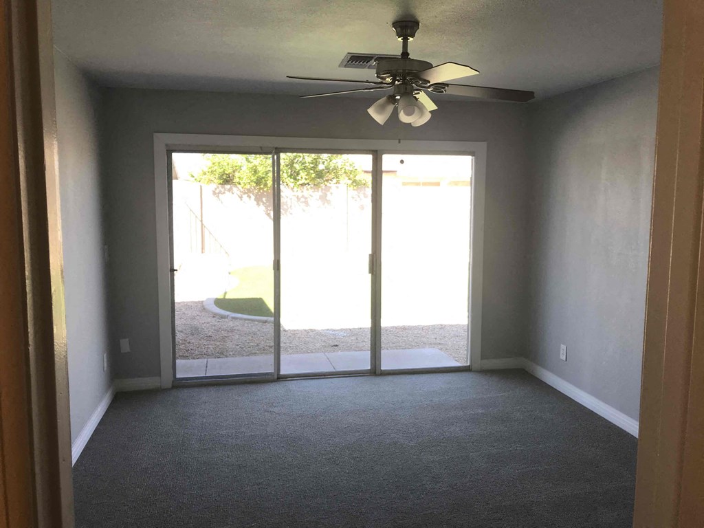 A room with a ceiling fan and sliding glass doors.