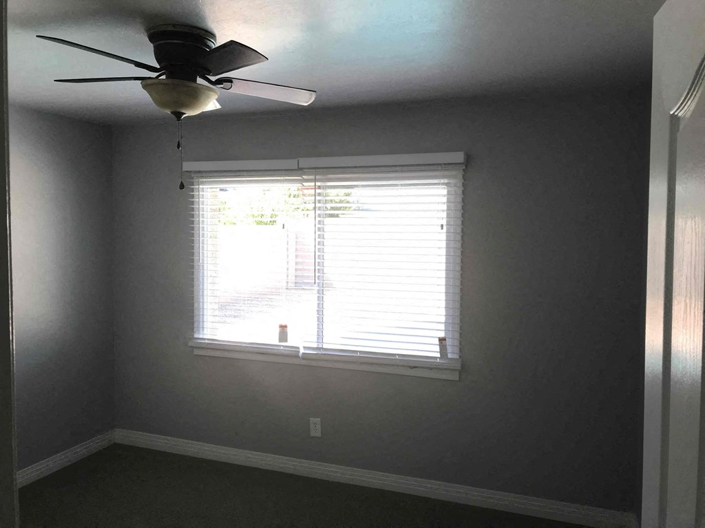 A room with a ceiling fan and a window with blinds.