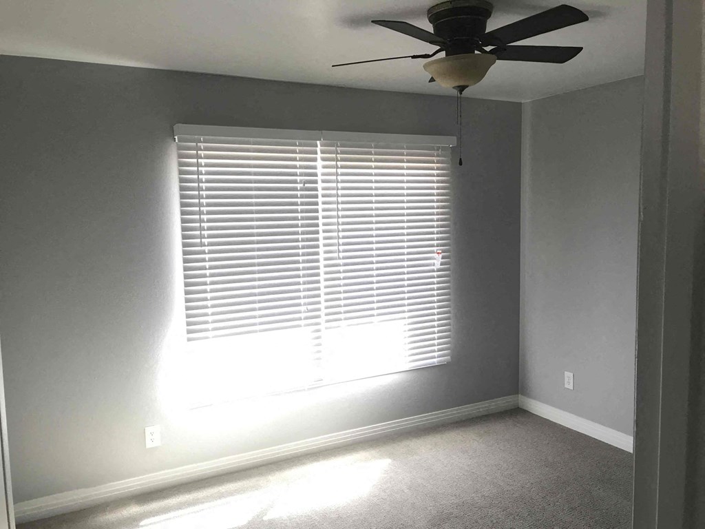 A room with a ceiling fan and a window with blinds.