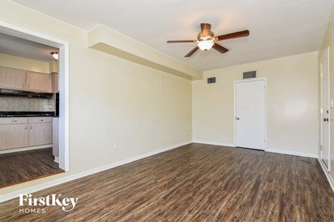 an empty living room with a ceiling fan and a kitchen