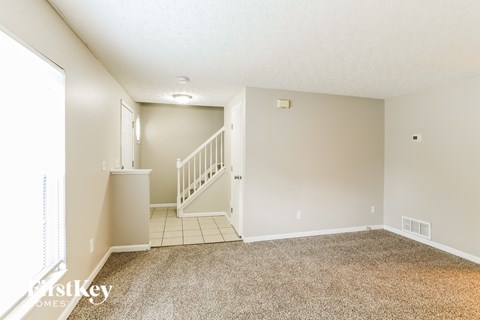 A carpeted room with a staircase leading to the second floor.