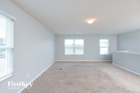 a spacious living room with white carpet and two windows