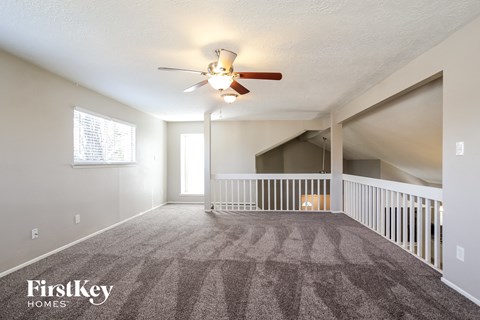 A spacious room with a carpeted floor and a ceiling fan.