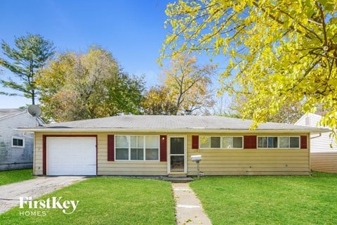 the front of a yellow house with a green lawn and trees